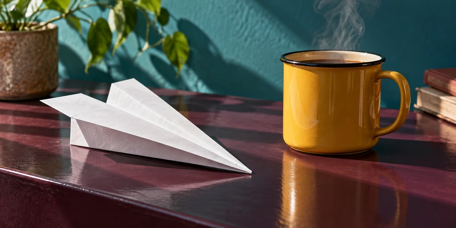 Avión de papel blanco junto a una taza humeante sobre una mesa