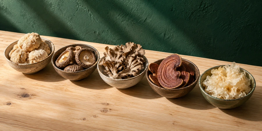 Setas secas de melena de león, shiitake, maitake, reishi y tremella en cuencos pequeños sobre una mesa de madera clara